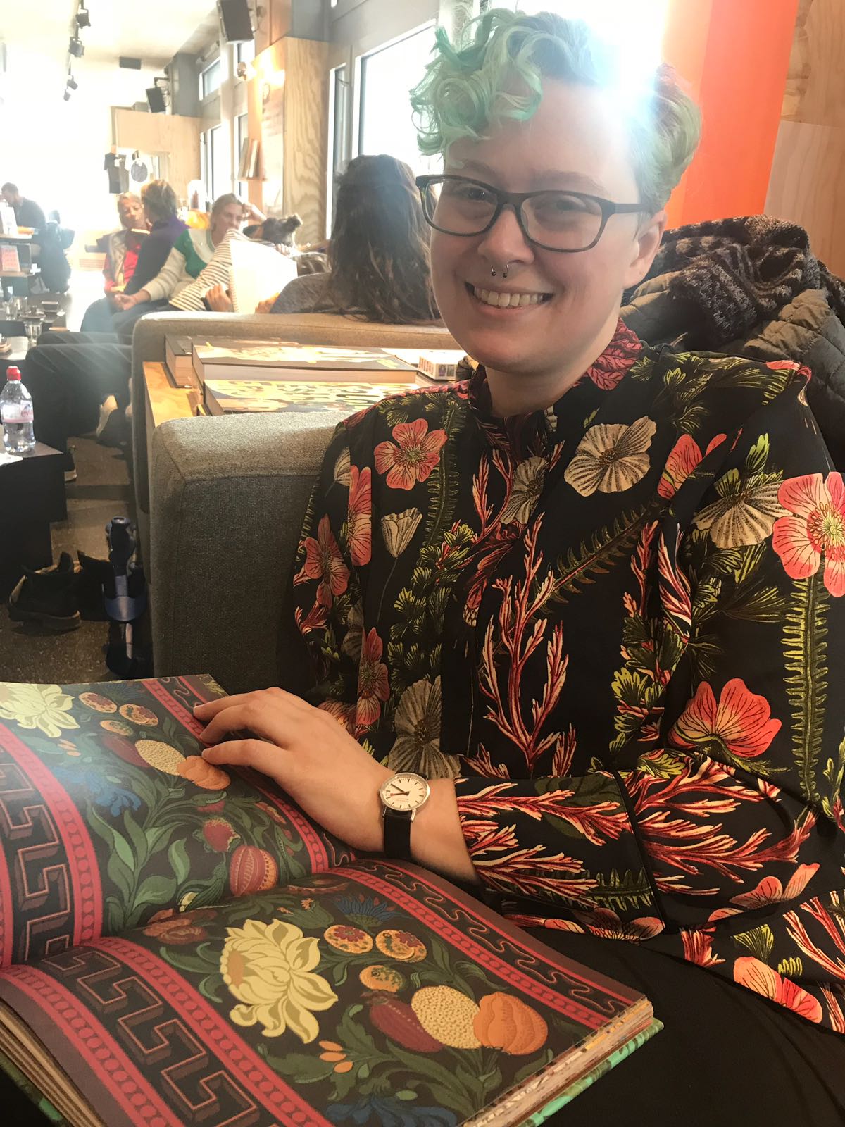 A person wearing a dark shirt with large green, white and red flowers printed on it, holding a book open to a very similar wallpaper design.
